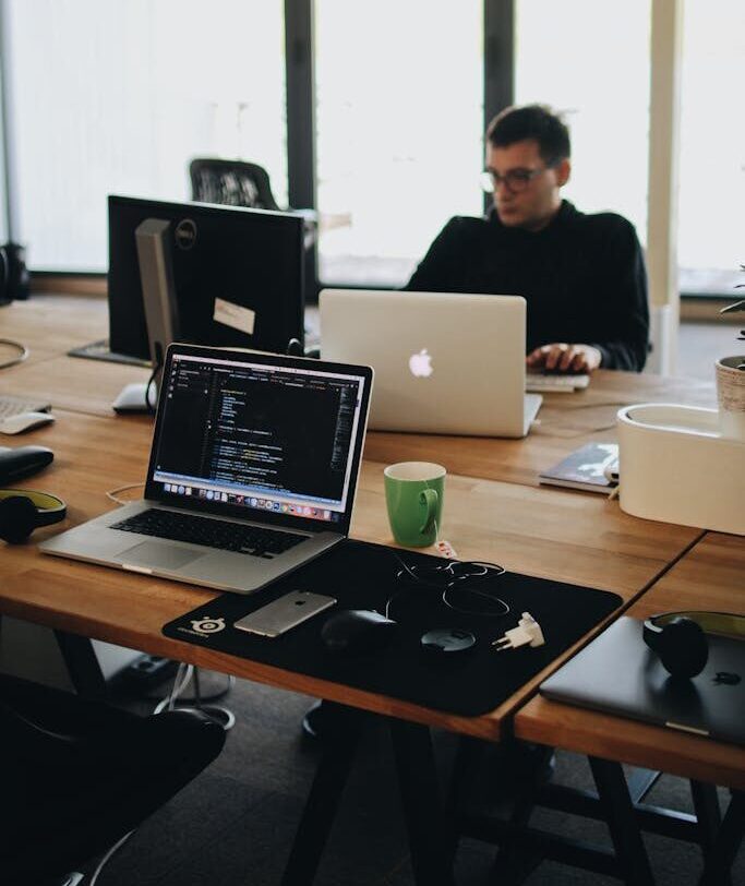 Man in Black Shirt Sits Behind Desk With Computers